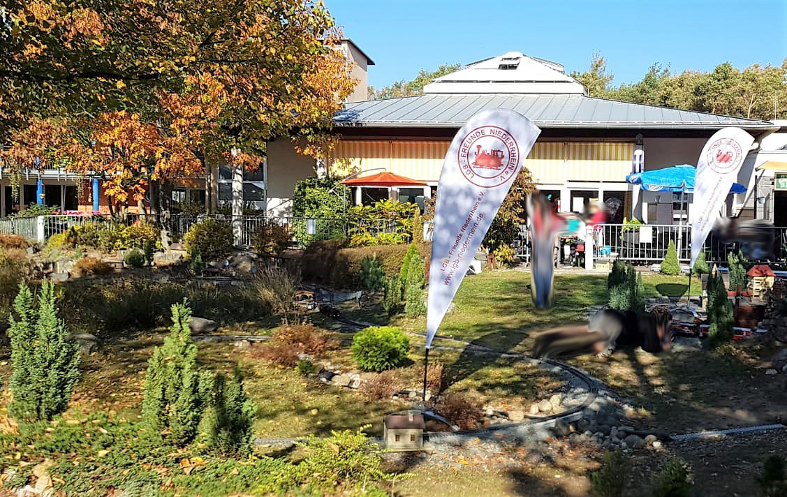 Blick ber die Gartenbahnanlage zum Ausstellungsraum. Die LGB Freunde Niederrhein e.V. machten durch Banner auf sich aufmerksam und waren mit einer Modulanlage im eigenen Ausstellungszelt bei den 10. Griesheimer Gartenbahntagen vor Ort.  