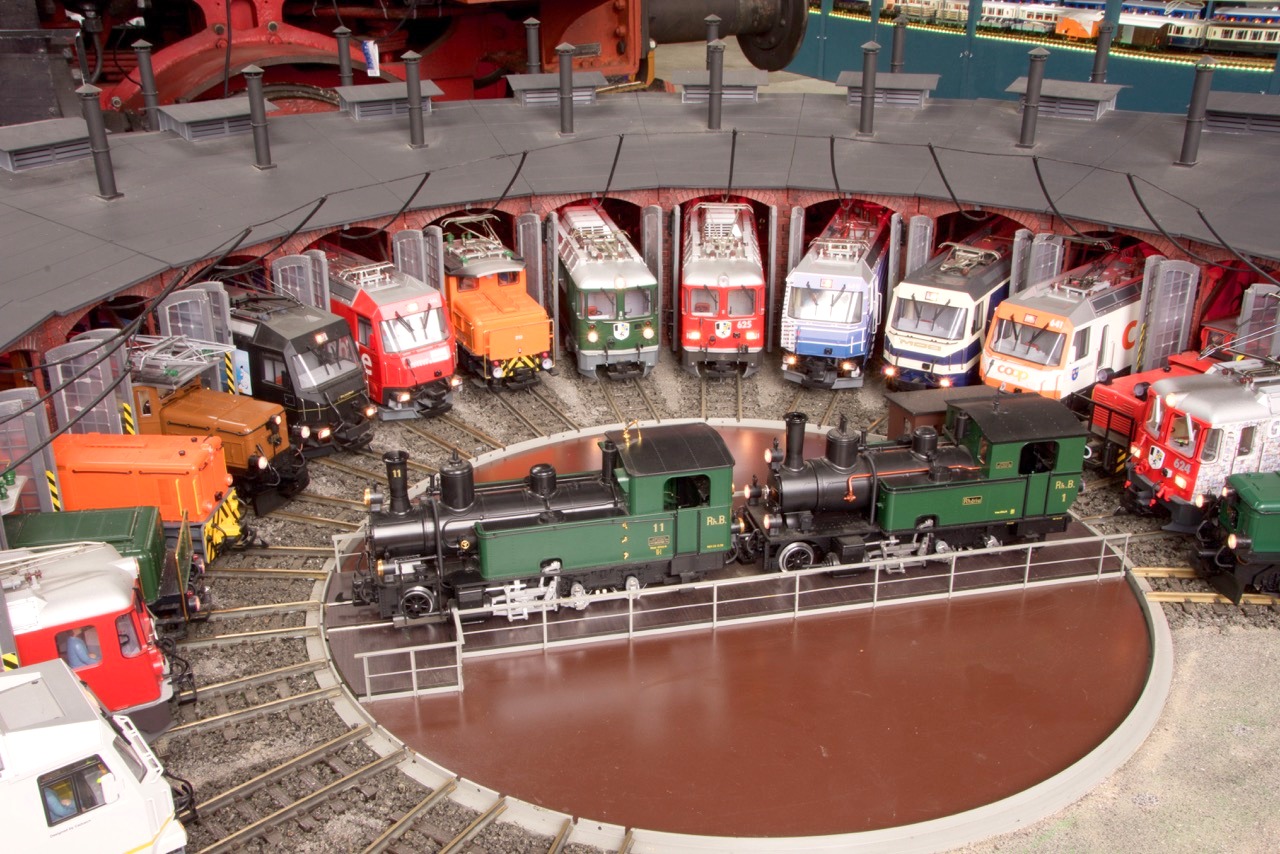 RhB Fahrzeuge - Aufgestellt im groen Ringlokschuppen im Bahnpark Augsburg. Auf der Bhne der Drehscheibe steht die Dampflok Nr. 11 - Heidi - und die Dampflok Nr. 1 - Rhtia. Zu erkennen sind auch einige Sonderlackierungen.