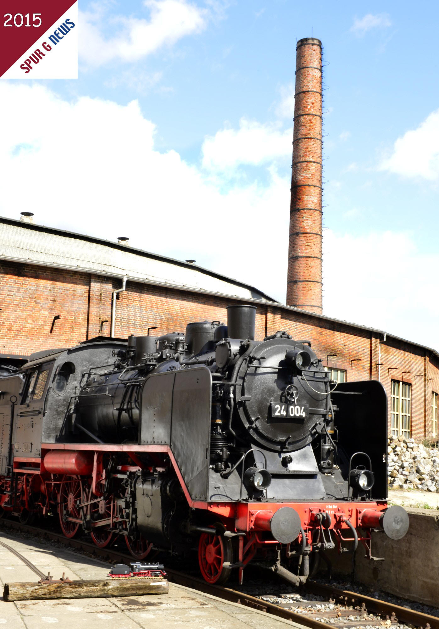 Bilderbuchwetter - eine Original BR 24 in einem Bahnbetriebswerk mit Ringlokschuppen aus Backsteinen sowie einem Fabrikschlot. Das Modell der BR 24 wurde auf einer alten Schwelle links neben dem Original zum fotografieren platziert. 