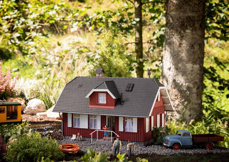 POLA 2024 - 331093 - Ferienhaus -  LTraditionelles Modell eines Ferienhauses in schwedenroter Holzverkleidung und einem dunkelgrauen, Ziegel gedeckten Walmdach mit zwei Dachgauben. Auf der Vorder- und Rckseite des Gebudes fhrt eine Auentreppe mit Gelnder zum Innenbereich. Die Tren sind beweglich