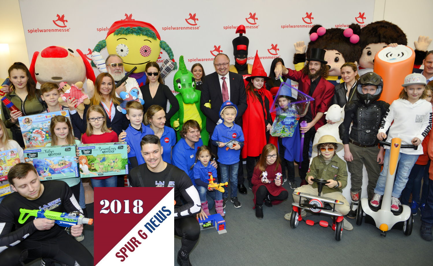 Ein Bild das zur Erffnung dazugehrt. Alle Kinder und lebensechte Puppen versammeln sich vor der Fotowand der Spielwarenmesse zum gemeinsamen Foto. In der Mitte der Vorstandsvorsitzende der Spielwarenmesse, Herr Ernst Kick.    