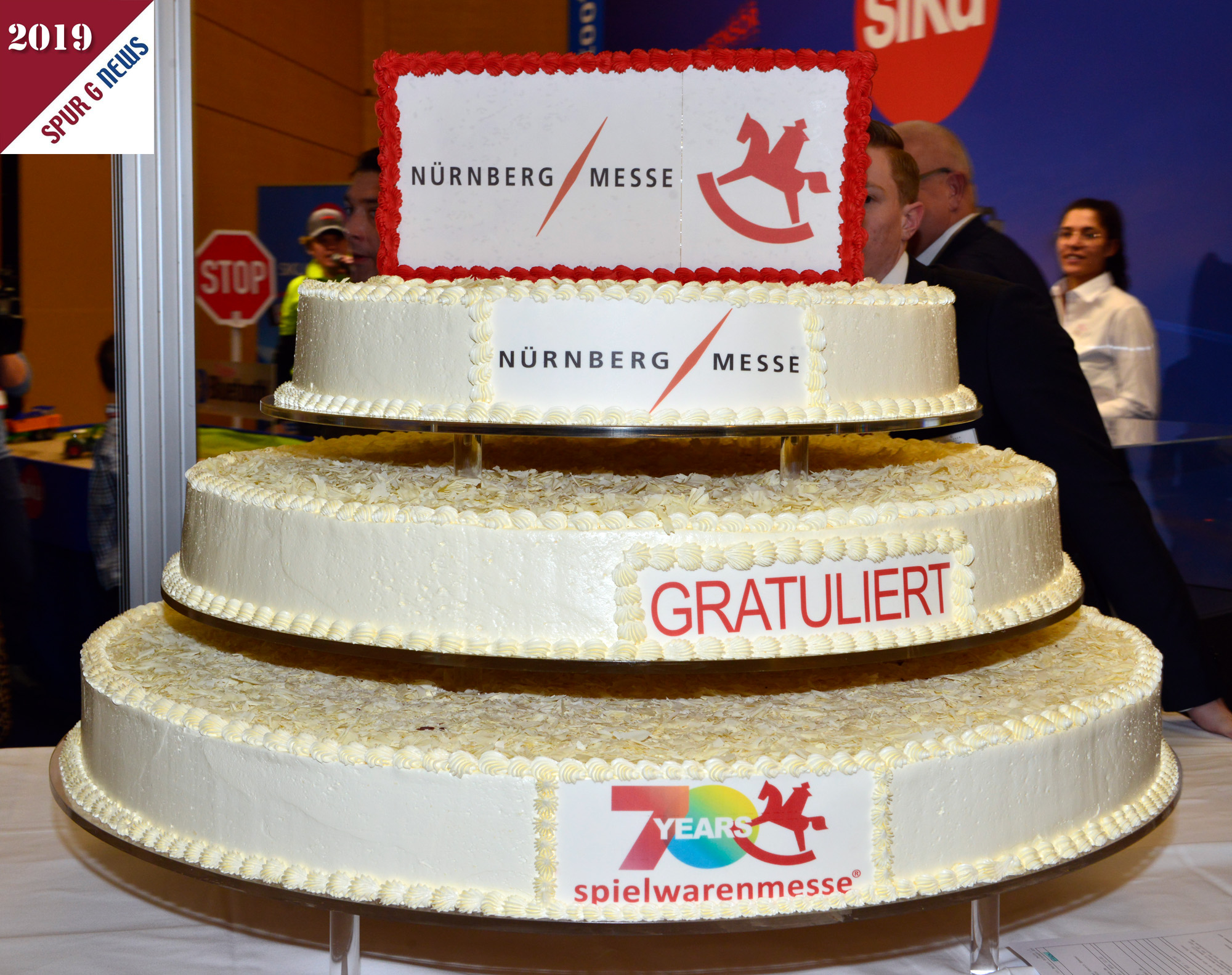 Heuer steht alles im Zeichen von 70 Jahren spielwarenmesse. Die dreistckige Torte wurde dann gegen Mittag von der Geschftsleitung der Messe Nrnberg an Herrn Kick, Vorstandsvorsizer der spielwarenmesse zum Anschnitt berreicht. Erdbeere, Champagner und Schokolade waren die drei Geschmacksrichtungen in den drei Etagen. Wir haben von den 70.000 Kalorien auch ein Stck verputzt. Natrlich Schokolade. Die Fanfarenblser der Stadt Nrnberg bliesen den Messeauftakt krftig mit den Fanfaren. 