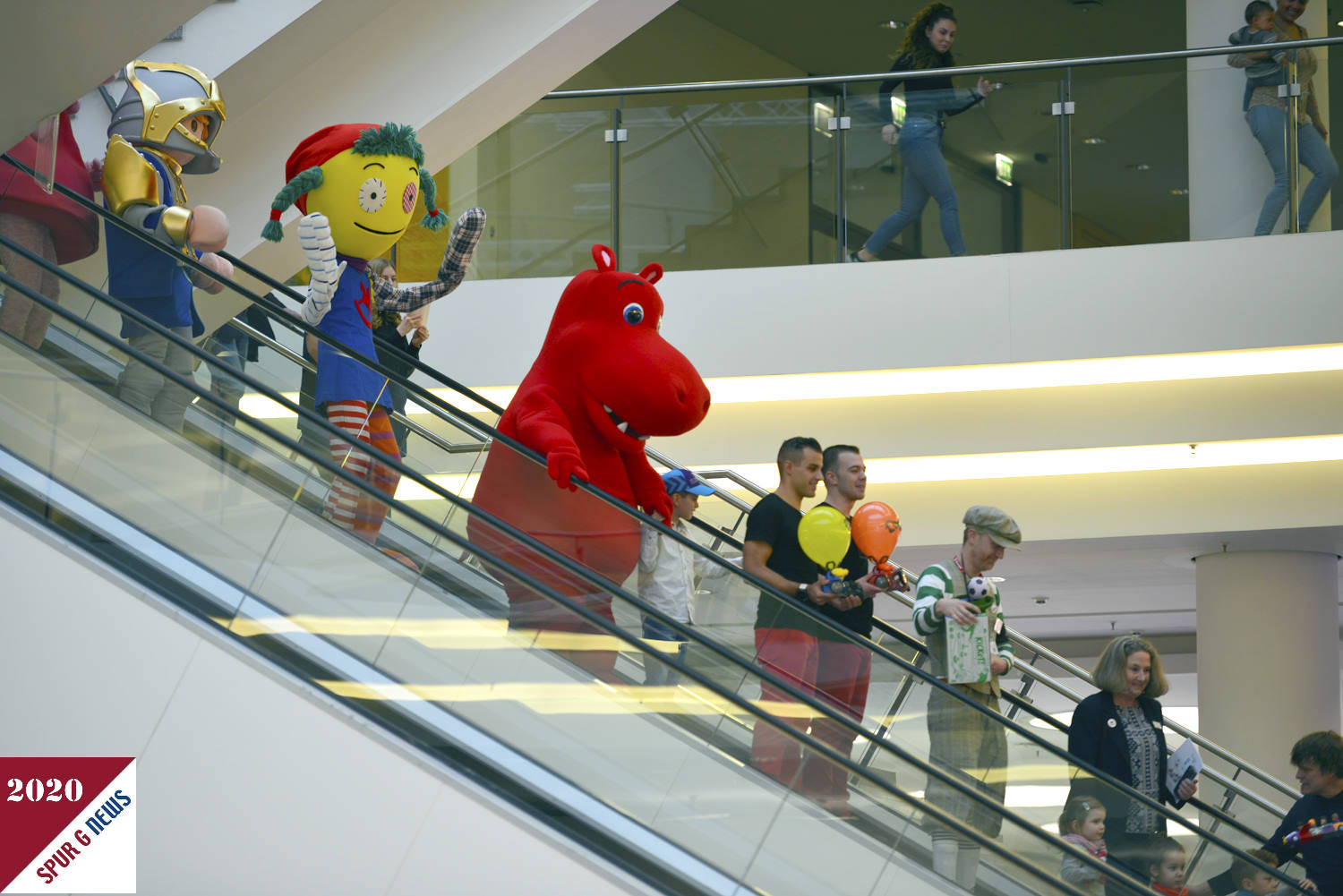 Hier sind die Walking Acts auf der Treppe vom 2. OG zur Rotunde unterwegs. Nach der Band waren auch die nominierten Firmen fr den ToyAward 2020 beim Marsch mit dabei. Zwischen dem roten Flupferd und der Novelmore Playmobilfigur luft (fhrt) das Walking Act Maskotchen der spielwarenmesse. 