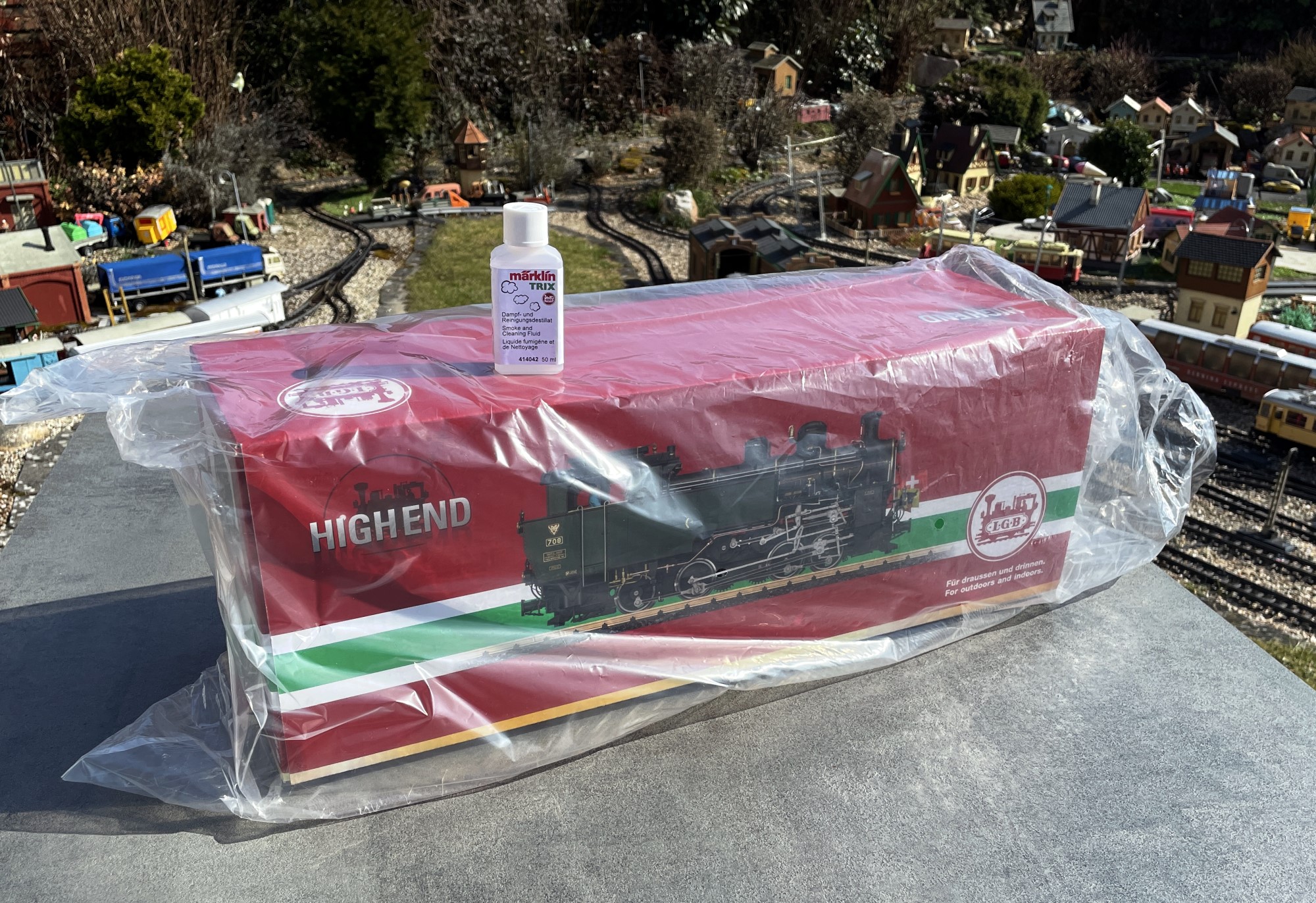 Im bräunlichen Umkarton ist neben den Styroporecken und Styroporteilen noch eine Flasche Dampfloköl zum Vorschein gekommen. Der übliche rote Karton mit der weiß-grün-weißen Bauchbinde war noch in Folie verpackt.