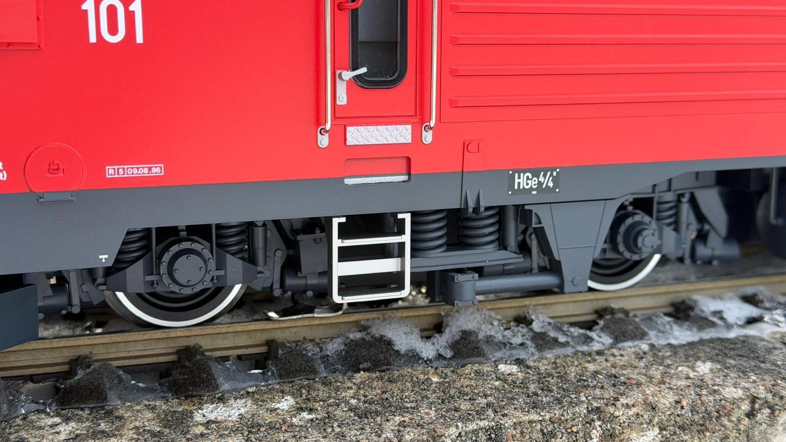 Detailaufnahme vom Einstieg in die HGe 4/4 II der FO Nr. 101 - Art. Nr. 23103 von LGB - Herbstneuheit 2025. Die Aufstiegsleiter sowie das Kantenblech unterhalb der Türe sind sehr gut nachgebildet und setzen durch die silberne Lackierung einen tollen Akzent an die Lok. Das Typenschild ist ebenfalls Originalgetreu angebracht. Als Revisionsdatum ist die Nr. 5 mit Datum 9.8.85 aufgedruckt. Somit ist diese Lok schon lange im Einsatz.