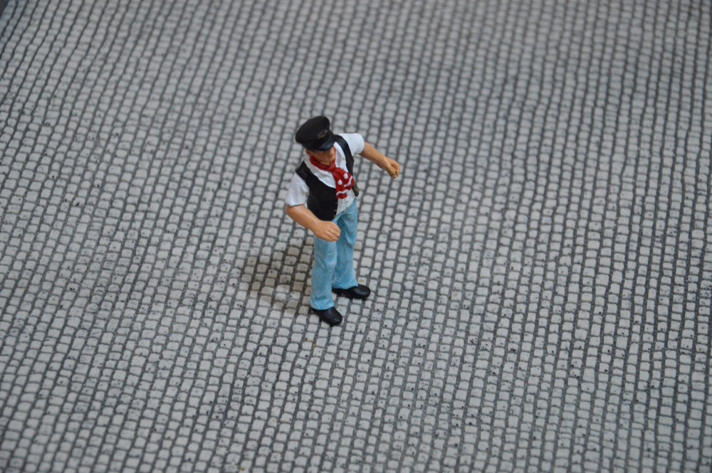 Auf die Kopfsteinpflastermatte wurde auf der Messe eine Metallfigur von Prehm-Miniaturen zum Größenvergleich gestellt. Bei Schuhgröße 43 des Miniaturmannes (haben wir angenommen), wäre dies ca. 30 cm Schuhlänge im Original. Somit wäre ein Pflasterstein ca. 10cm in der Wirklichkeit breit/lang. Dies entspricht einem guten Granitpflaster wie es auch vor Hauseingängen oder Geschäften verlegt wird.
