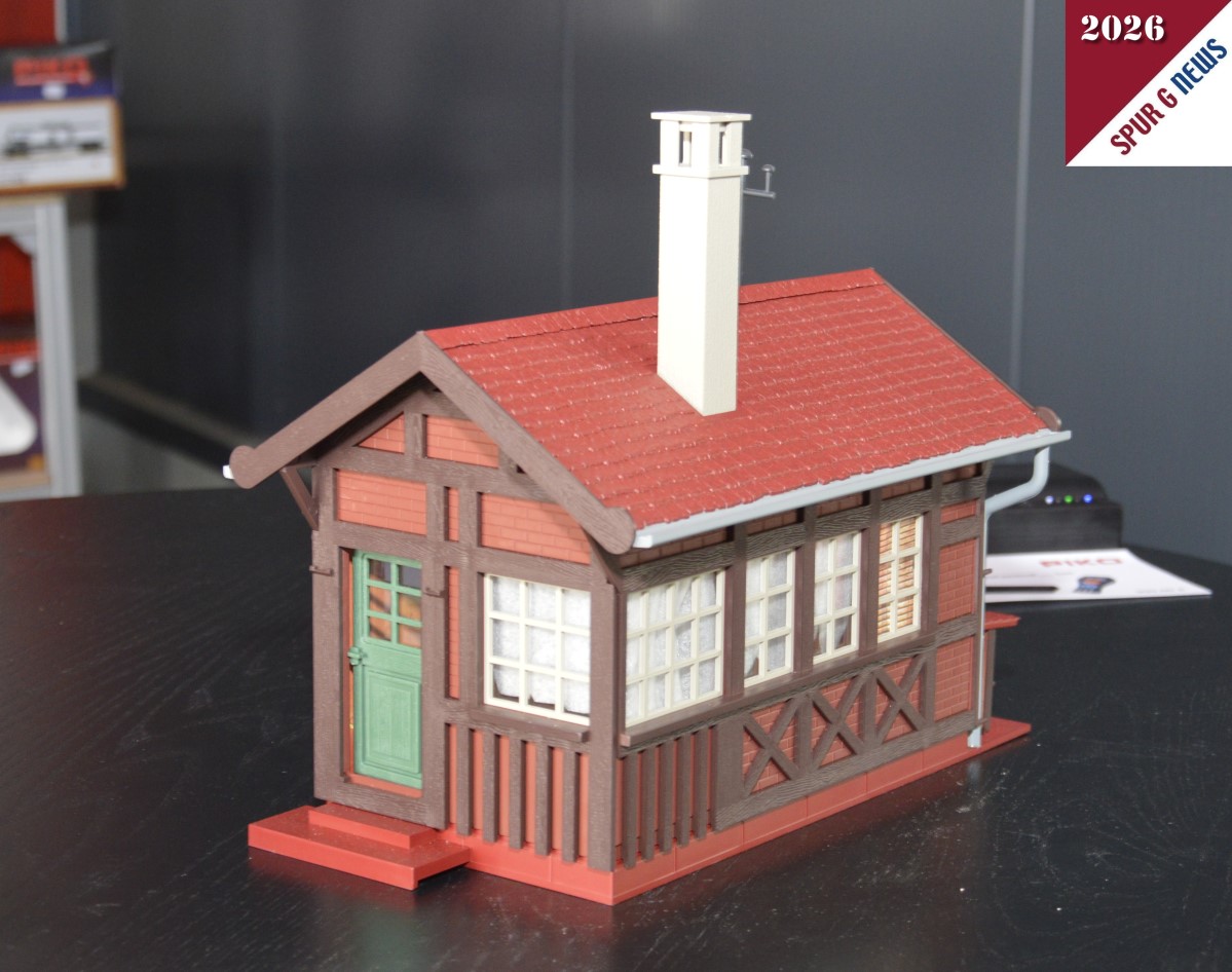 Das Bahnwärterhaus - Art. Nr. 65002 - konnten wir auf dem Präsentiertisch fotografieren. Link der Eingang des Hauses und rechts der Hinterhof mit dem gestapelten Holz unter der kleinen Überdachung. Sicherlich ragt der Kamin im Vorbild des Bahnwärterhauses auch so in die Höhe. Im Prospekt ist das Fachwerk weiß abgebildet. Hier beim Start in die Gartenbahnsaison sind es Klinkersteine die zwischen den aufgesetzten Balken eingebaut sind. Auch die Dachrinnen sind hier im Muster grau dargestellt. Im Prospekt grün. Wir werden erneut darüber berichten.