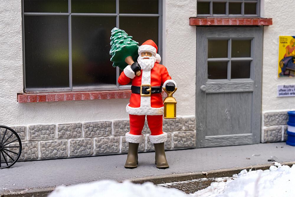 POLA Art. Nr. 331537 - Weihnachtsmann - Weihnachtsmann Weihnachtliche Stimmung! Mit rotem Mantel, schwarzem G�rtel und warm gef�tterten Stiefeln steht der Weihnachtsmann bereit f�r seinen winterlichen Einsatz. �ber der Schulter tr�gt er einen kleinen schneebedeckten Tannenbaum, in der anderen Hand h�lt er eine leuchtende Laterne � bereit, Licht in die dunkle Jahreszeit zu bringen. Ob auf dem Weg zum Weihnachtsfest oder als Teil einer festlichen Szene: Diese Figur bringt weihnachtliche Atmosph�re in jede Modelllandschaft. Ideal f�r Szenen im Dorf, an Marktpl�tzen oder auf verschneiten Wegen!